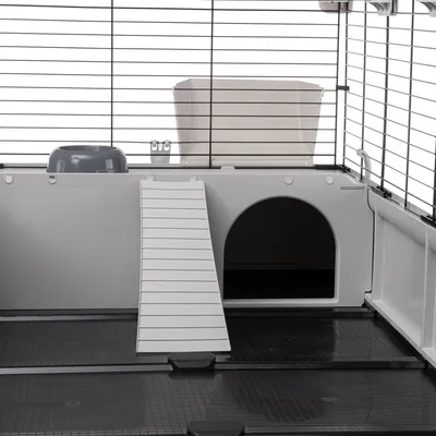 Kleintierkäfig mit weisser Rampe, grauem Futternapf und abgetrenntem Bereich mit Eingang. Metallgitter oben für Belüftung.