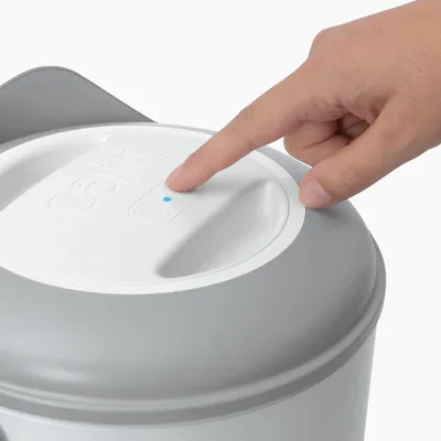 Finger presses the button on a white and grey device with the label 'Catit'. Blue LED indicator is lit.