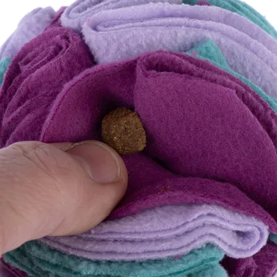 En hånd placerer en godbid i et legetøj af farverigt filt med lag af lilla, violet og grøn stof.