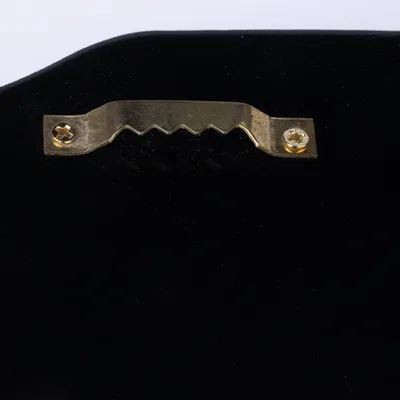 Primer plano de un colgador de metal dorado con borde dentado, fijado a una superficie negra.