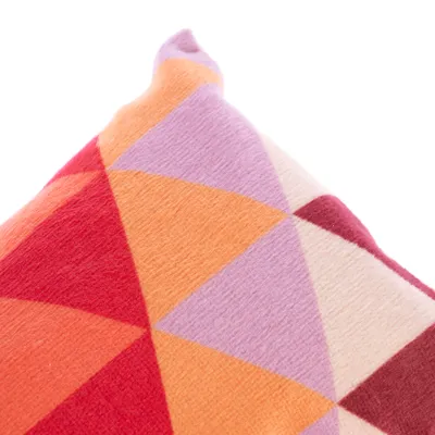 Detailní záběr na polštář s geometrickým vzorem v červené, oranžové, fialové a krémové barvě.