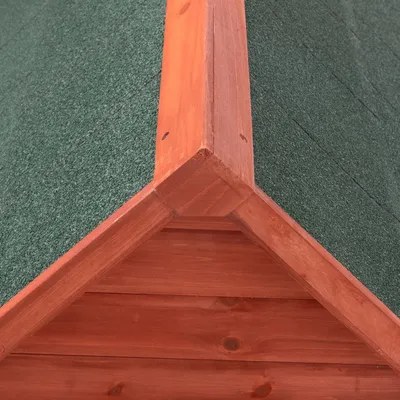 Toit en bois avec revêtement vert, vue rapprochée du faîte d’une niche ou abri pour animaux. Matériaux visibles : bois et surface texturée verte.