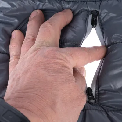 Main ouvrant une fermeture éclair sur un tissu matelassé gris, montrant l'intérieur du matériau. Fermeture éclair noire visible.