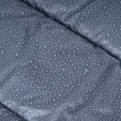 Nahaufnahme eines wasserabweisenden Materials mit sichtbaren Wassertropfen auf grauer Oberfläche.