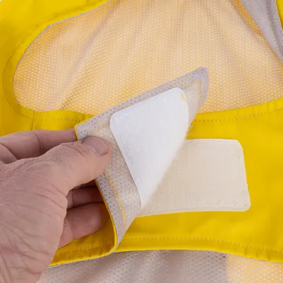 Gros plan sur une main ouvrant une fermeture à scratch sur un tissu jaune et beige, matière synthétique visible.