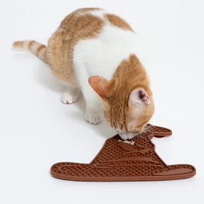 Braune Schleckmatte in Form eines Hutes, verwendet von einer rot-weissen Katze zum Fressen.