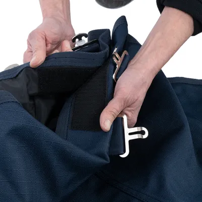 Nahaufnahme einer blauen Tasche mit Metallhaken und Klettverschluss, die von Händen geöffnet wird.