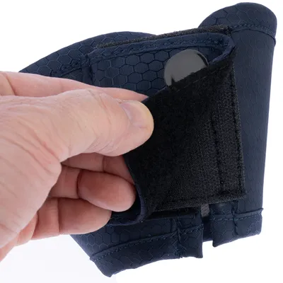 Gros plan sur une main ouvrant la fermeture velcro d’un accessoire bleu foncé à motif hexagonal, tissu visible et bouton noir apparent.