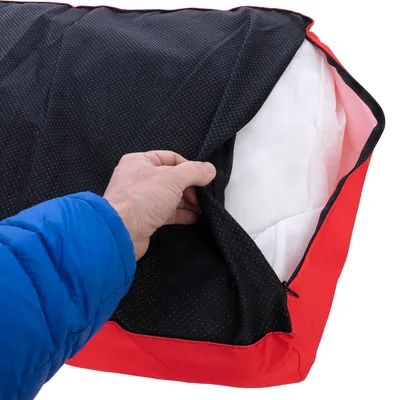 Main soulevant la housse noire à fermeture éclair d’un coussin pour animaux, montrant l’intérieur blanc du coussin. Housse en tissu noir et rouge.