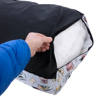 Main ouvrant la housse d’un coussin pour animaux, montrant l’intérieur blanc et la fermeture éclair sur le côté. Housse à motifs colorés visibles sur le bord.