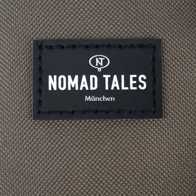 Nomad Tales München. Metka marki na brązowej tkaninie.