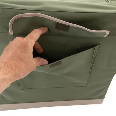 Bolso verde con cierre de velcro, una mano abre el compartimento exterior. Vista detallada de la funcionalidad del espacio de almacenamiento.