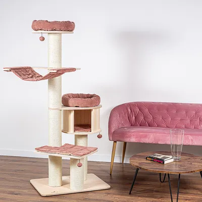 Kratzbaum aus Holz mit rosa Polsterungen, mehreren Ebenen, Hängematte und Höhle. Steht neben einem rosa Sofa und Holztisch in modernem Raum.