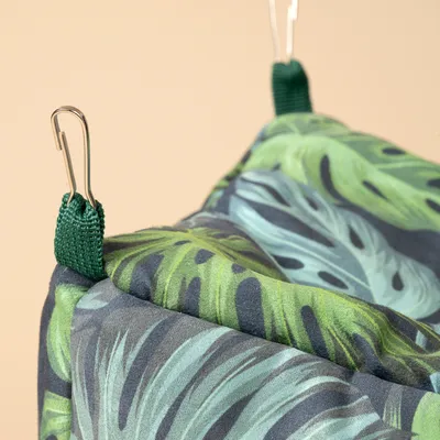 Hangmat met groen bladmotief, bevestigd met metalen haken en groene stoffen lussen.