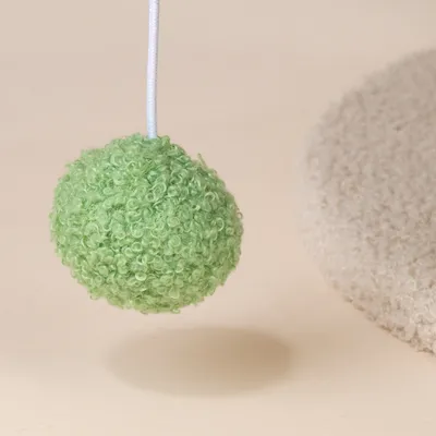 Zielona piłka do zabawy z tkaniny o teksturowanej powierzchni, przymocowana do białego sznurka.