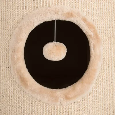 Circular entrance with soft plush trim and a hanging fluffy ball toy inside, set against a woven textured surface. Shows play and entry feature of the product.
