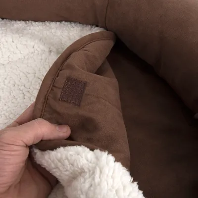 Nahaufnahme eines braunen Stoffbezugs mit weissem Plüschfutter und Klettverschluss, gehalten von einer Hand.