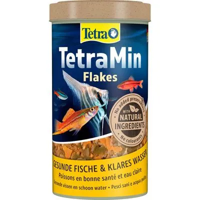 Tetra TetraMin Flakes visvoer, tekst: 'With natural ingredients', 'No added preservatives', 'No colourants', 'GESUNDE FISCHE & KLARES WASSER', zichtbaar vlokkenvoer en aquariumvissen.