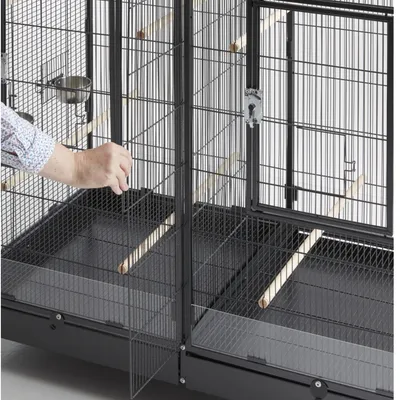 Colivie neagră pentru păsări cu grilaj metalic, bețe din lemn și bază detașabilă. O mână deschide o ușă mică în față.