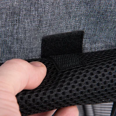 Nahaufnahme eines Klettverschlusses an einem grauen Stoff und schwarzem Netzmaterial, gehalten von einer Hand.