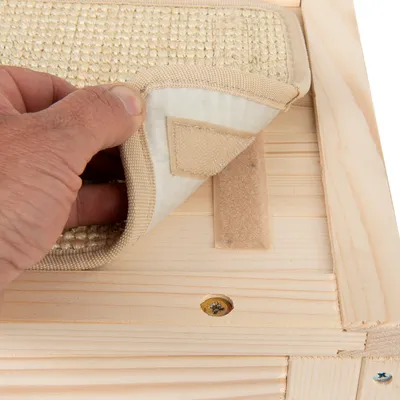 Hand hebt beige Kratzmatte mit Klettverschluss von einer Holzoberfläche an, zeigt Befestigungsmethode.