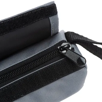 Detailní pohled na šedou tašku s zipem a suchým zipem z odolného materiálu. Viditelný černý popruh.