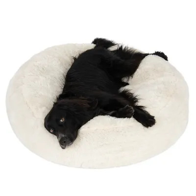 Black dog lying on a large, round, fluffy white pet bed, demonstrating the size and comfort of the product.