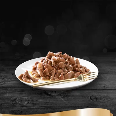 Annos ruskeita kastikkeessa olevia lihapaloja valkoisella lautasella, vieressä kultainen haarukka. Tuotemerkki tai pakkaus ei näy.