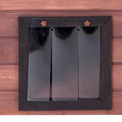 Plastična vrata za kućicu za pse s tri prozirne trake i crnim okvirom, montirana na drvenu površinu.