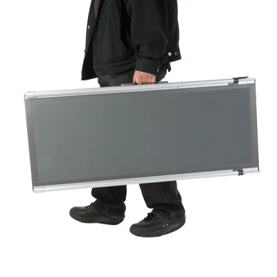 Opgevouwen metalen draagbare hondenloopplank, rechthoekig model met handvat, wordt gedragen door een persoon in zwarte kleding en schoenen.