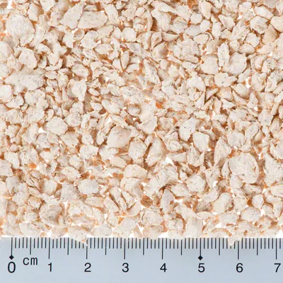 Close-up of light brown flakes with a ruler in centimetres for size reference. Flake size approximately 0 to 5 mm.