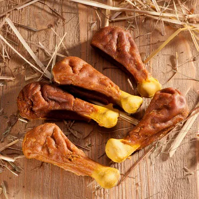 Fem hundgodisbitar formade som kycklingben på träunderlag med halm. Inga synliga varumärken eller förpackning.