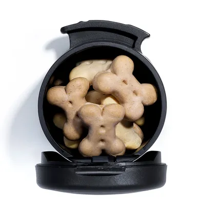 Boîte noire ouverte contenant des biscuits en forme d’os pour chien, vue de dessus. Les biscuits sont de couleur beige clair et empilés à l’intérieur du récipient.