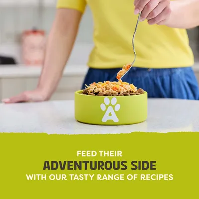 Person puts food into a green bowl with a paw print and the letter A. Text: Feed their adventurous side with our tasty range of recipes.