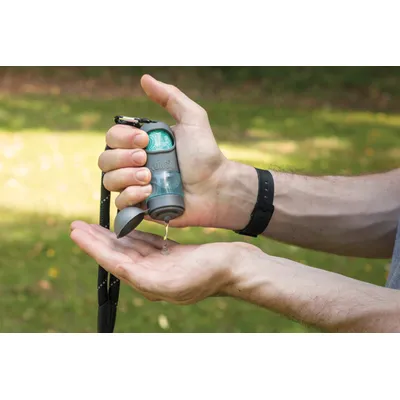 Osoba wyciska płyn z pojemnika KONG do dłoni; w środku widoczna rolka woreczków. Pojemnik z tworzywa, z karabińczykiem i otwartą klapką.