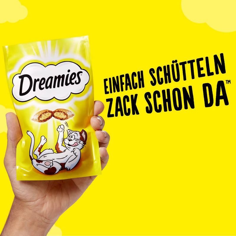 Dreamies kattegodbidder i gul pose, tekst på tysk: 'Einfach schütteln zack schon da'. Katteillustration og to godbidder vist på emballagen.