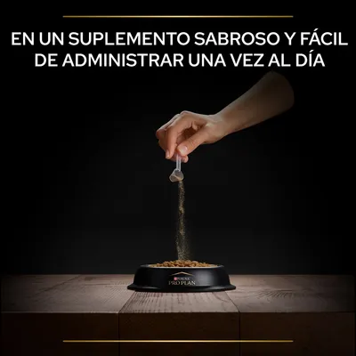 Texto: En un suplemento sabroso y fácil de administrar una vez al día. Mano vertiendo polvo sobre pienso en cuenco negro Purina Pro Plan.