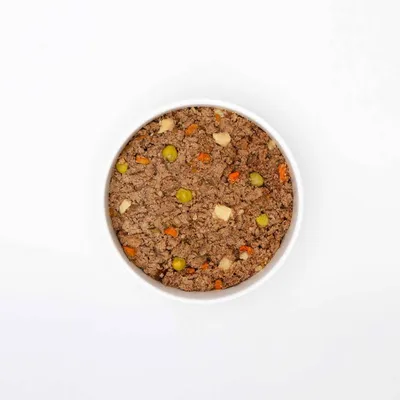 Bowl filled with minced pet food containing visible pieces of vegetables such as peas and carrots.