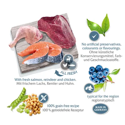 Saumon, viande de renne et poulet frais sur planche, pois, pois chiches, myrtilles, feuilles. Textes visibles : 100 % recette sans céréales, Made in Germany, All fresh, With fresh salmon, reindeer and chicken.