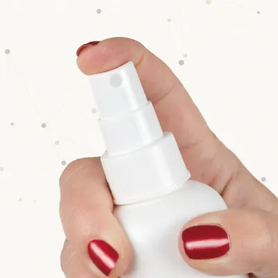 Hand mit roten Nägeln drückt auf weißen Sprühkopf einer Flasche. Detailaufnahme des Sprühmechanismus.