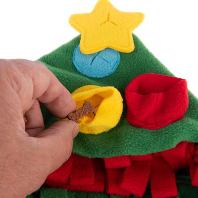 Ręka wkłada smakołyk do żółtej kieszeni zielonej zabawki z czerwonymi i niebieskimi kieszeniami oraz żółtą aplikacją w kształcie gwiazdy.