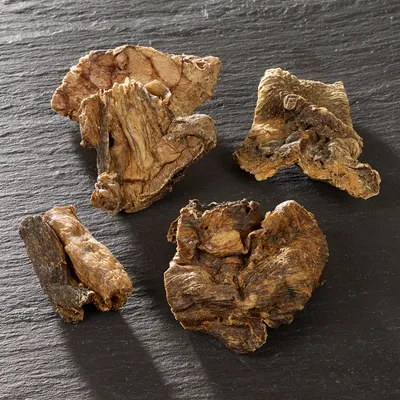 Morceaux de friandises séchées pour animaux, aspect brun et irrégulier, posés sur une surface noire. Aucun emballage ou marque visible.