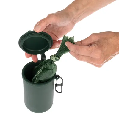 Contenant vert en plastique avec couvercle ouvert, une main y place un sac vert noué. Mousqueton noir fixé sur le côté du contenant.