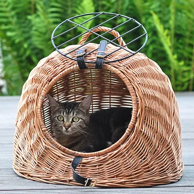 Cesta para gatos de mimbre trenzado con rejilla metálica superior y cierre de correa de cuero. Gato sentado dentro de la cesta.