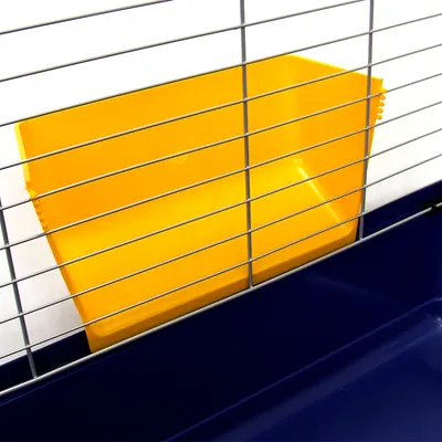Bac d’angle jaune en plastique fixé à l’intérieur d’une cage à barreaux métalliques, fond de la cage bleu foncé visible.