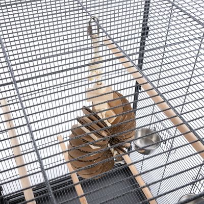 Cage en métal avec perchoirs en bois, jouet suspendu en corde, carton et bois, et deux gamelles métalliques fixées aux barreaux.
