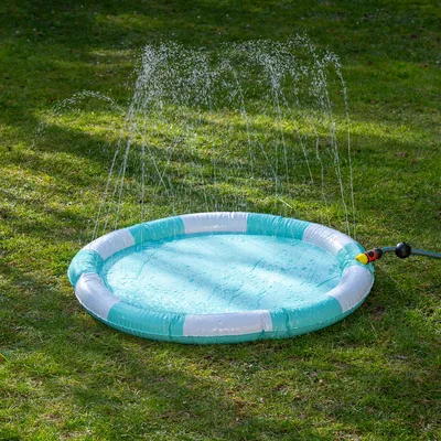 Rundes, türkis-weisses Wasserspielzeug mit Sprinklerfunktion, angeschlossen an einen Gartenschlauch. Wasserstrahlen sprühen nach oben auf einer grünen Rasenfläche.