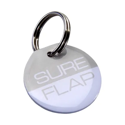 Rund nøglebrik med teksten SURE FLAP, fastgjort til en metalnøgle-ring. Materiale: plastik og metal.