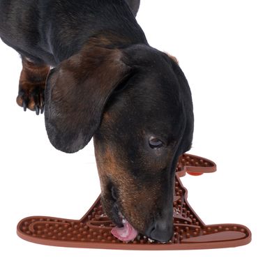 Куче ближе кафява постелка за близане във форма на кост с релефна повърхност, подходяща за занимание или хранене.