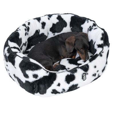 Cane sdraiato in un letto per cani con rivestimento in peluche a motivo nero-bianco. Logo 'Trixie' visibile sul bordo del letto.